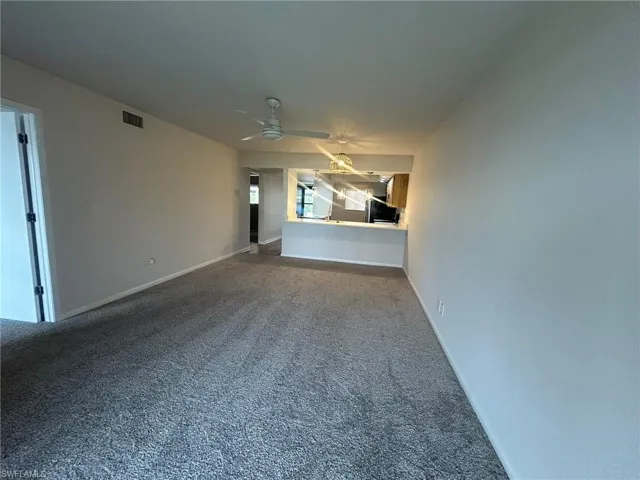 Unfurnished living room with carpet floors, baseboards, visible vents, and ceiling fan