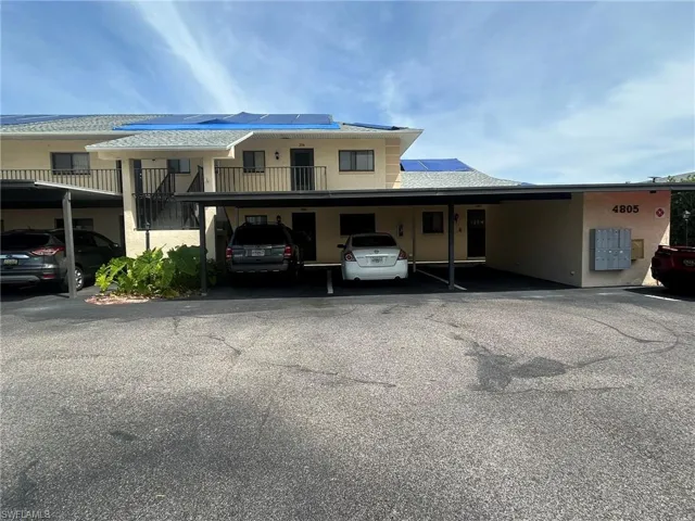 View of front of property featuring covered parking, roof mounted solar panels, stucco siding, and roof with shingles