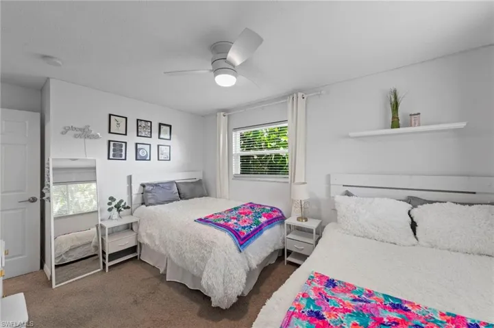 Room featuring two white bed frames, a window with blinds, a ceiling fan, and a built-in wall shelf