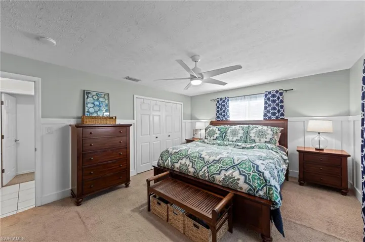 Carpeted flooring, paneled wainscoting, a ceiling fan with integrated lighting, and white bi-fold closet doors