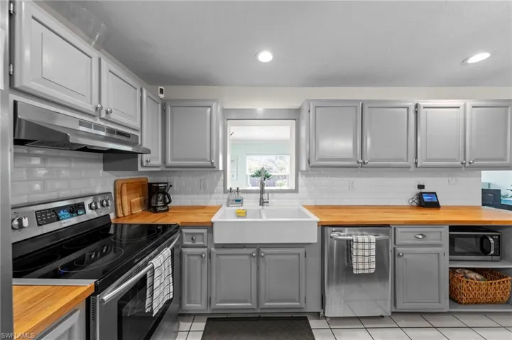 Kitchen featuring shaker-style cabinetry, wood-finish countertops, subway tile backsplash, a farmhouse sink, and stainless steel appliances