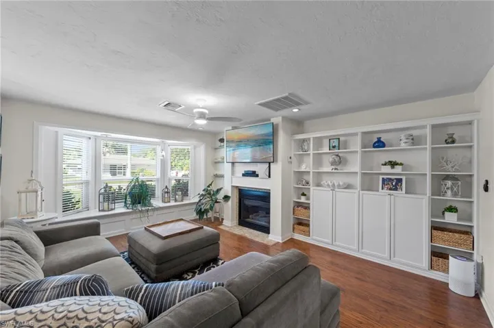 Hardwood-finish flooring, built-in shelving, bay window, ceiling fan, and a fireplace with a mantel