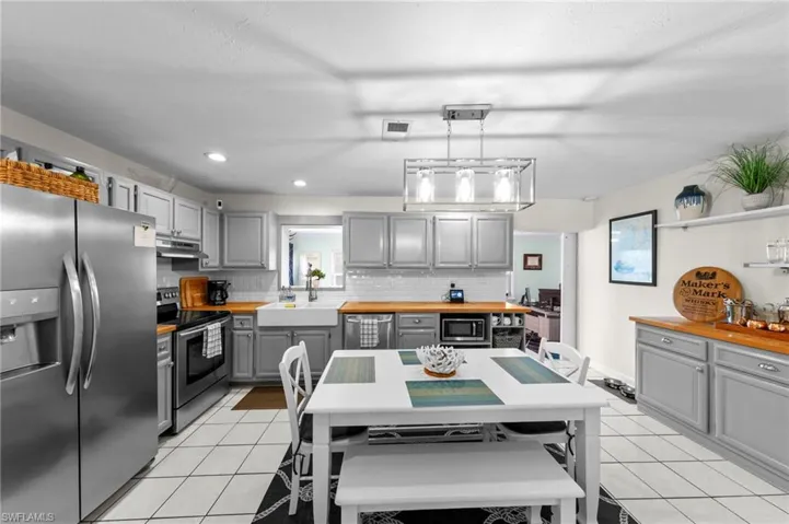 Stainless steel appliances, wood-finish countertops, white subway tile backsplash, white farmhouse sink, and recessed lighting