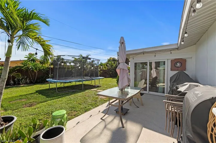 Expansive backyard featuring a manicured lawn, established palm trees, and a concrete patio with string lighting