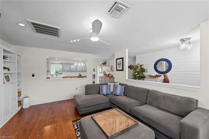 Hardwood-finish flooring, built-in shelving, ceiling fan with integrated lighting, recessed lighting, and a pass-through window to the kitchen