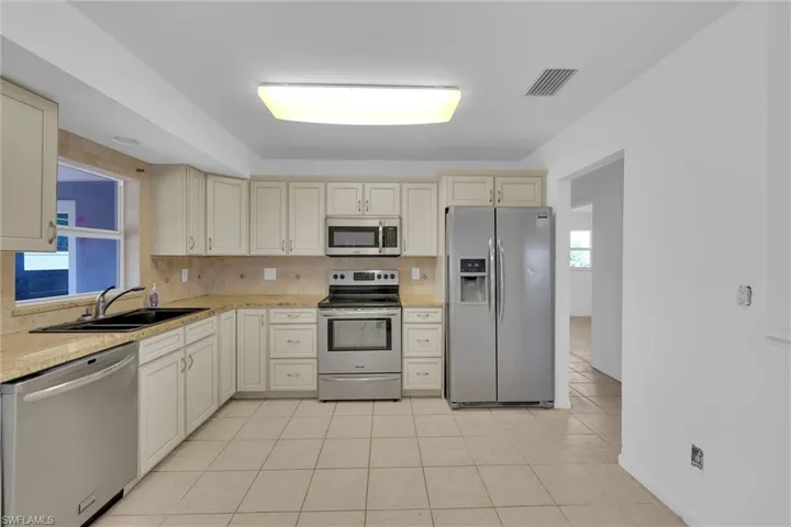 Kitchen with cream cabinets, stainless steel appliances, light tile patterned floors, and decorative backsplash