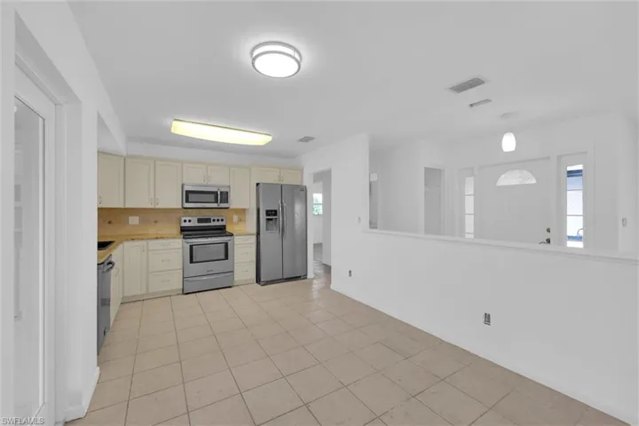 Kitchen with cream cabinets, stainless steel appliances, decorative backsplash, light countertops, and light tile patterned floors