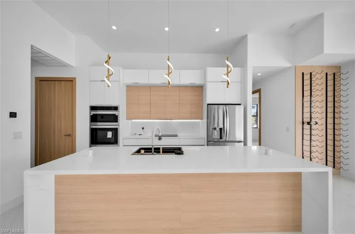 Kitchen with sink, white cabinetry, decorative light fixtures, appliances with stainless steel finishes, and a kitchen island with sink