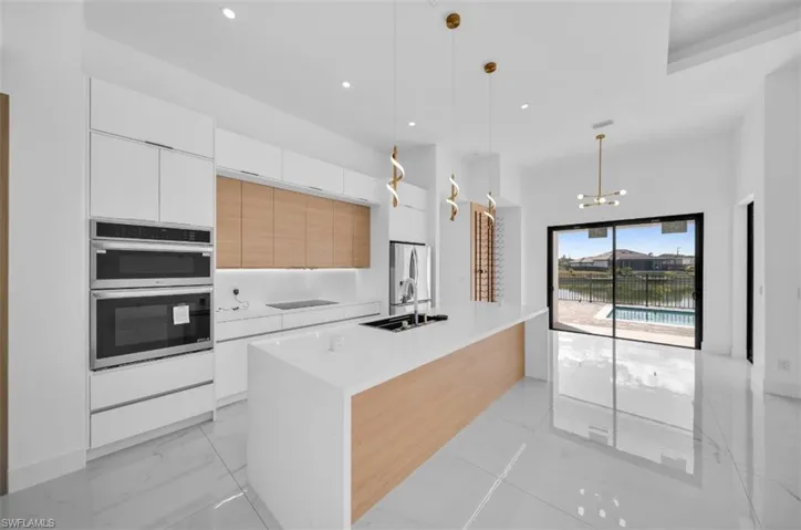 Kitchen with white cabinetry, sink, decorative light fixtures, and a kitchen island with sink