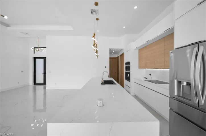 Kitchen featuring decorative light fixtures, sink, white cabinets, light stone counters, and stainless steel refrigerator with ice dispenser