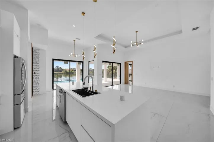 Kitchen featuring white cabinetry, sink, hanging light fixtures, a kitchen island with sink, and an inviting chandelier