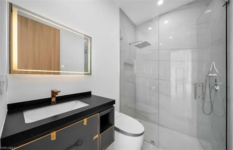 Bathroom featuring a shower with door, vanity, and toilet