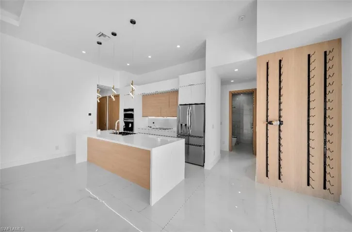 Kitchen featuring sink, white cabinetry, decorative light fixtures, a center island with sink, and appliances with stainless steel finishes