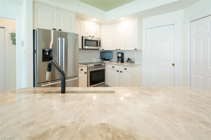 Kitchen featuring white cabinetry, light stone counters, stainless steel appliances, and backsplash