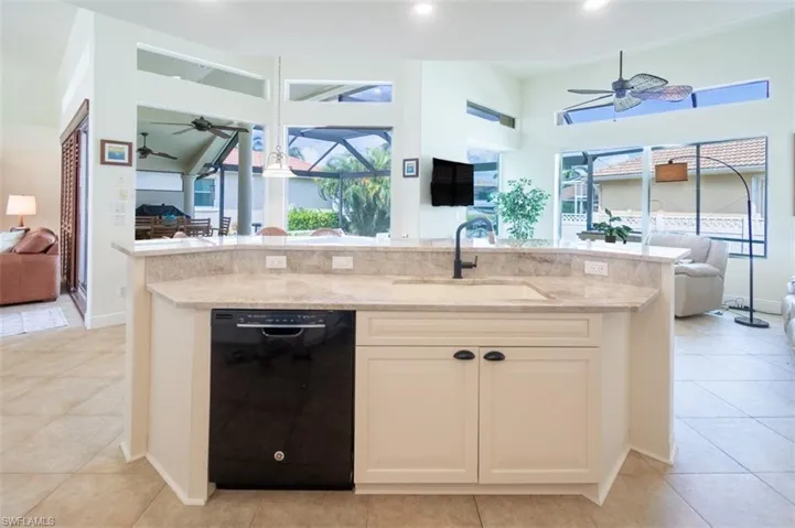 Kitchen with black dishwasher, sink, light stone countertops, light tile patterned floors, and ceiling fan