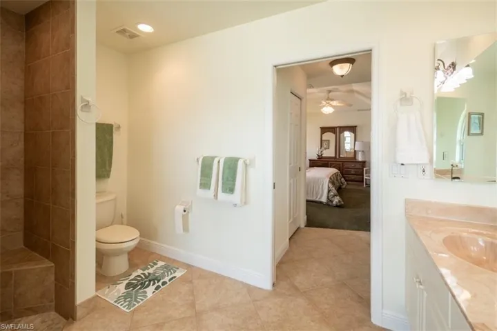 Bathroom with a tile shower, toilet, ceiling fan, tile patterned floors, and vanity