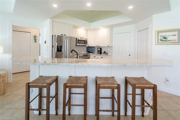 Kitchen featuring light stone countertops, appliances with stainless steel finishes, a kitchen bar, and white cabinets