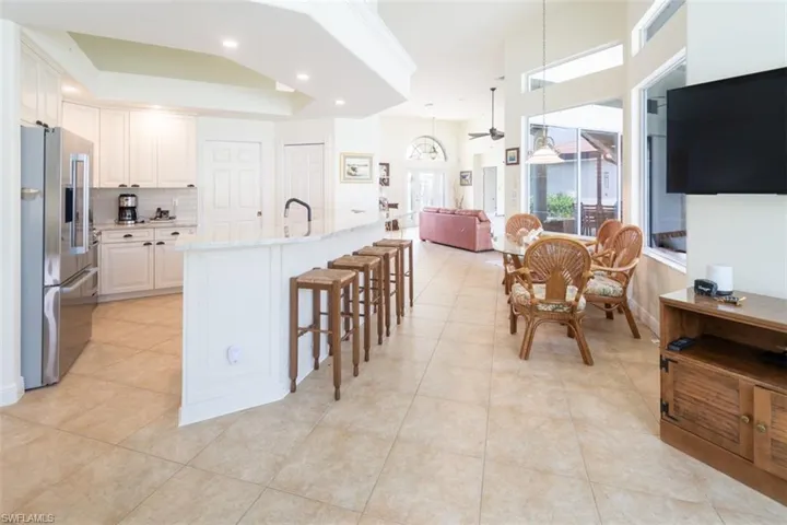 Kitchen with light stone counters, white cabinetry, a kitchen island with sink, stainless steel refrigerator with ice dispenser, and decorative light fixtures