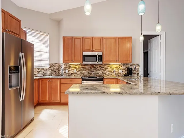 Kitchen with sink, hanging light fixtures, stainless steel appliances, kitchen peninsula, and lofted ceiling