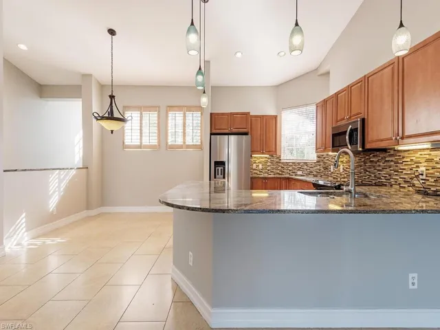 Kitchen featuring kitchen peninsula, appliances with stainless steel finishes, hanging light fixtures, and dark stone countertops