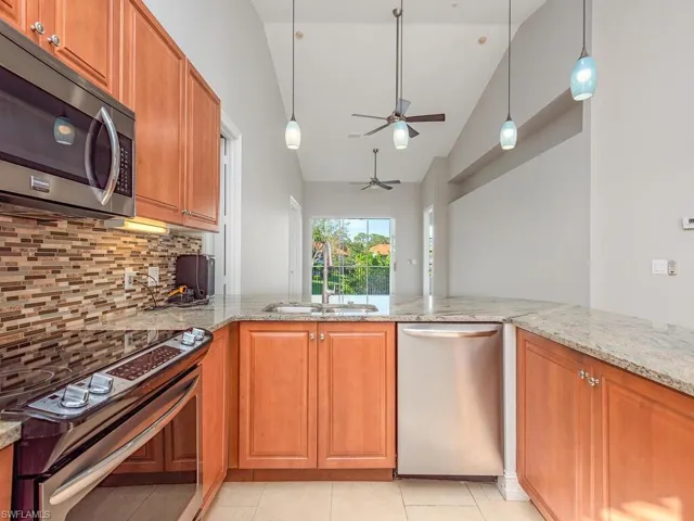 Kitchen with ceiling fan, sink, stainless steel appliances, light stone counters, and high vaulted ceiling