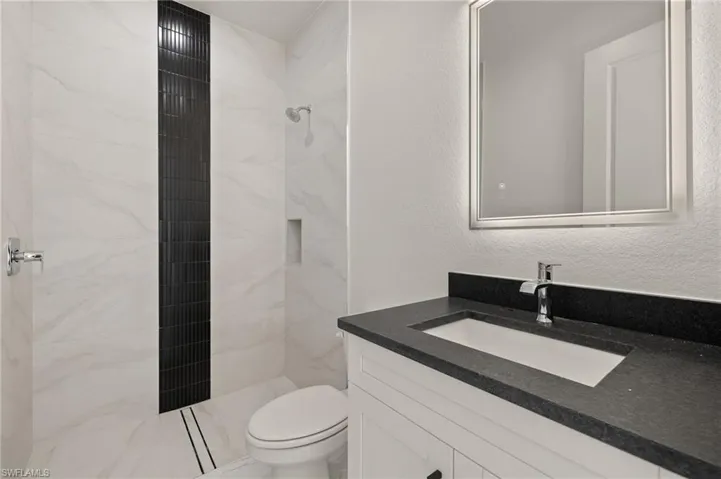 Bathroom with a tile shower, vanity, and toilet