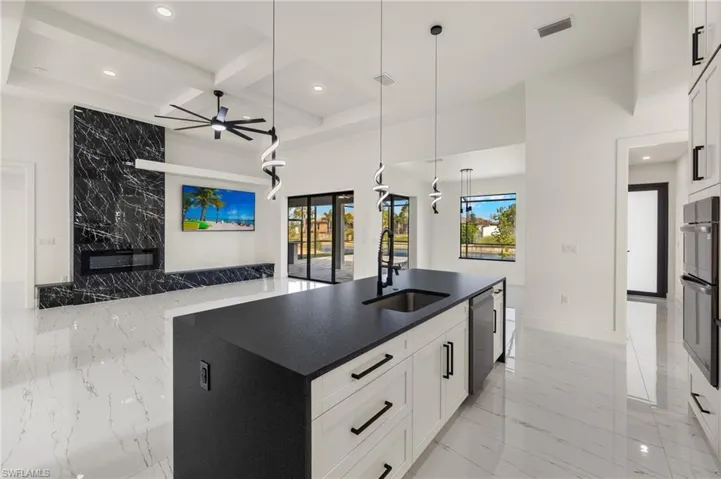 Kitchen with white cabinetry, sink, hanging light fixtures, coffered ceiling, and an island with sink