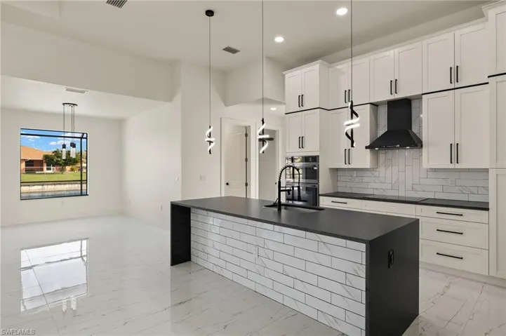 Kitchen featuring a center island with sink, white cabinetry, hanging light fixtures, and wall chimney exhaust hood