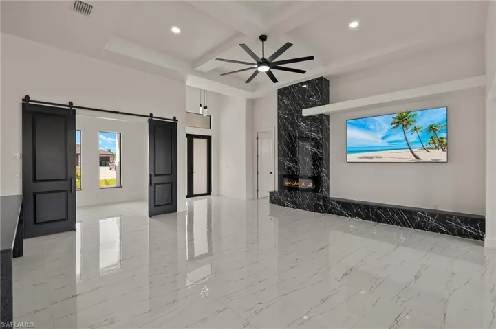 Unfurnished living room featuring beamed ceiling, a barn door, ceiling fan, and coffered ceiling