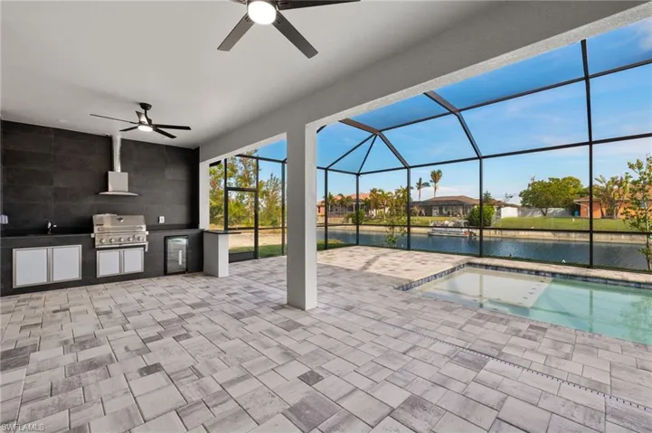 View of patio / terrace featuring a water view, ceiling fan, a lanai, a grill, and exterior kitchen