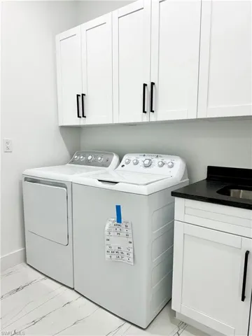 Laundry area with washer and dryer, cabinet space, marble finish floor, and a sink