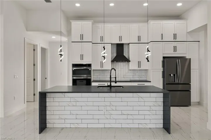 Kitchen featuring backsplash, white cabinetry, wall chimney range hood, and stainless steel appliances