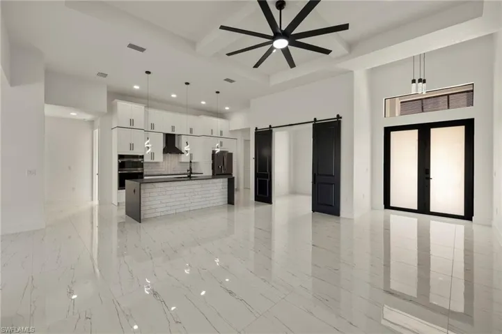 Kitchen featuring exhaust hood, hanging light fixtures, a barn door, an island with sink, and white cabinetry