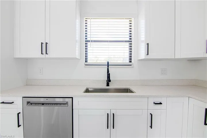 Kitchen with dishwasher, light stone counters, and white cabinetry