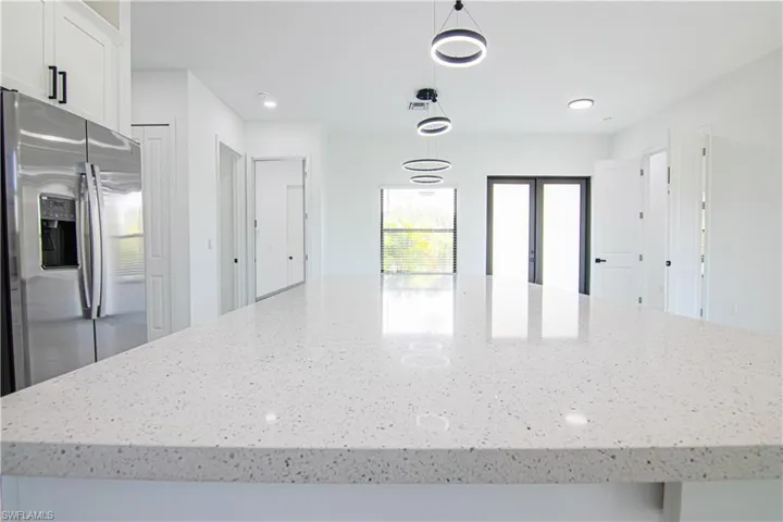 Kitchen featuring stainless steel refrigerator with ice dispenser, decorative light fixtures, white cabinetry, recessed lighting, and light stone counters