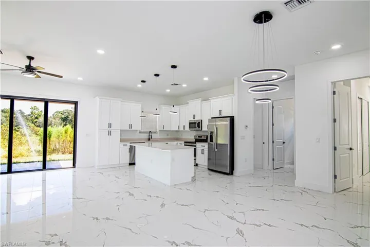 Kitchen featuring light marble finish flooring, white cabinetry, hanging light fixtures, stainless steel appliances, and a center island