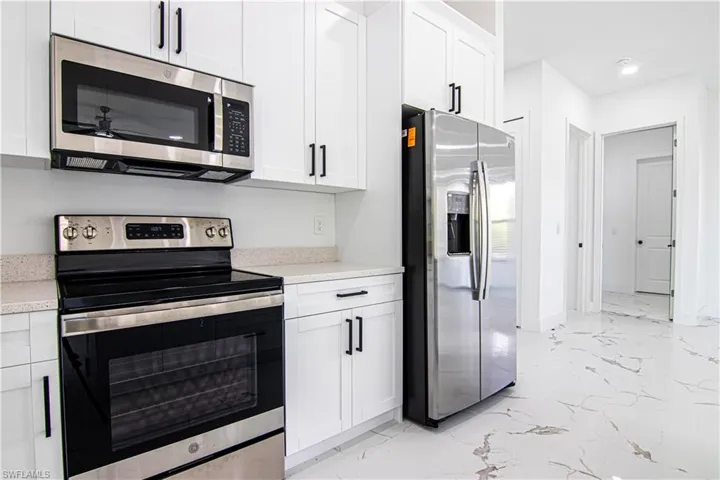 Kitchen featuring stainless steel appliances, light marble finish floors, white cabinetry, and light stone countertops