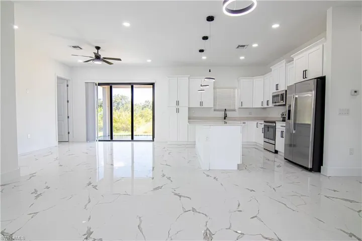 Kitchen with light marble finish flooring, stainless steel appliances, open floor plan, white cabinetry, and recessed lighting
