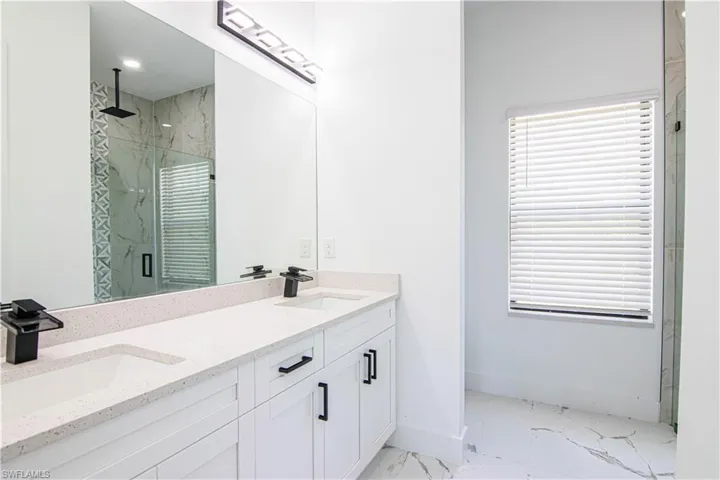 Full bath with light marble finish flooring, a marble finish shower, and double vanity
