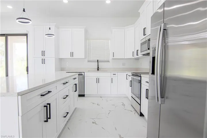 Kitchen with appliances with stainless steel finishes, light marble finish flooring, white cabinetry, a center island, and pendant lighting