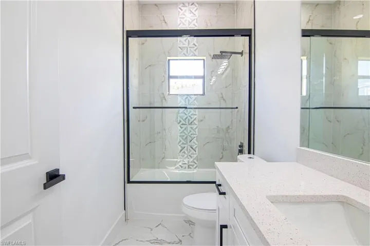 Full bathroom featuring light marble finish floors, enclosed tub / shower combo, and vanity