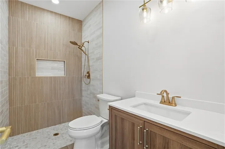 The bathroom features a walk-in shower with textured wall tiles, a recessed shower shelf, and a gold-toned shower fixture - Virtually Edited Image