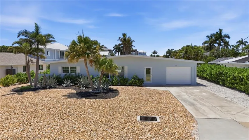 The property features a light-colored exterior, a garage with a white door, and a paved driveway - Virtually Edited Image