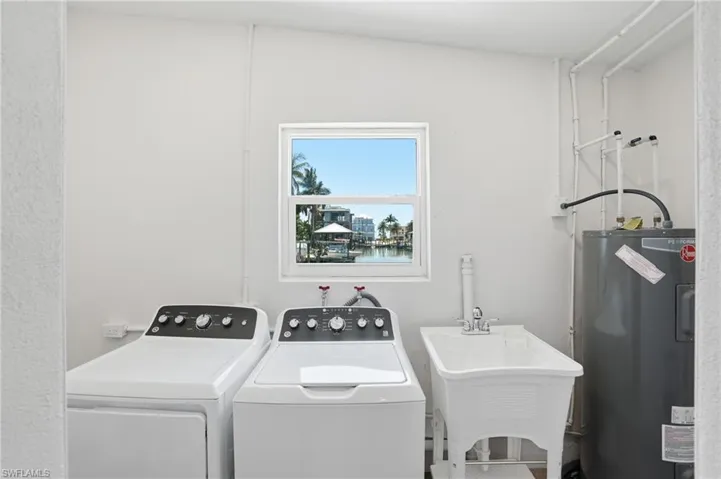 Utility room featuring a window with a water view, a laundry sink, and a water heater - Virtually Edited Image