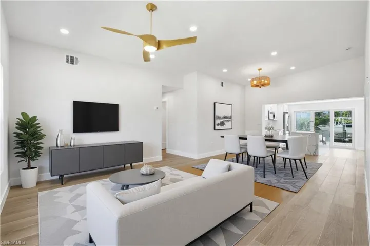 Bright and open living area featuring light-colored flooring, recessed lighting, and a vaulted ceiling with a modern ceiling fan - Virtually Edited Image
