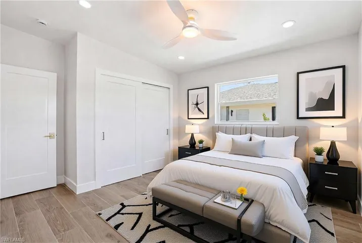 This bedroom features light wood-look flooring, a window providing natural light, and a ceiling fan with integrated lighting - Virtually Edited Image