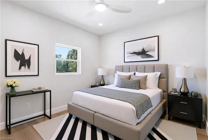 The bedroom features light wood flooring, a window providing views of greenery, and a ceiling fan with integrated lighting - Virtually Edited Image