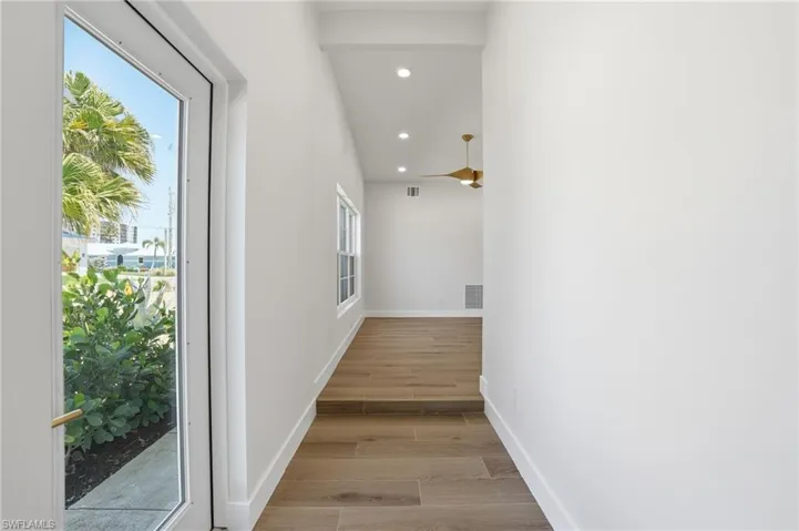 Inviting entry with light-toned flooring, crisp white walls, and a large glass-paned door offering natural light and views of tropical foliage - Virtually Edited Image
