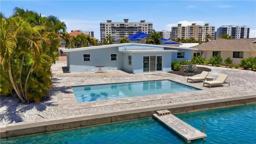 Exterior view of the property featuring room for a private swimming pool, a concrete patio area, and direct access to a body of water via a small dock - Virtually Edited Image