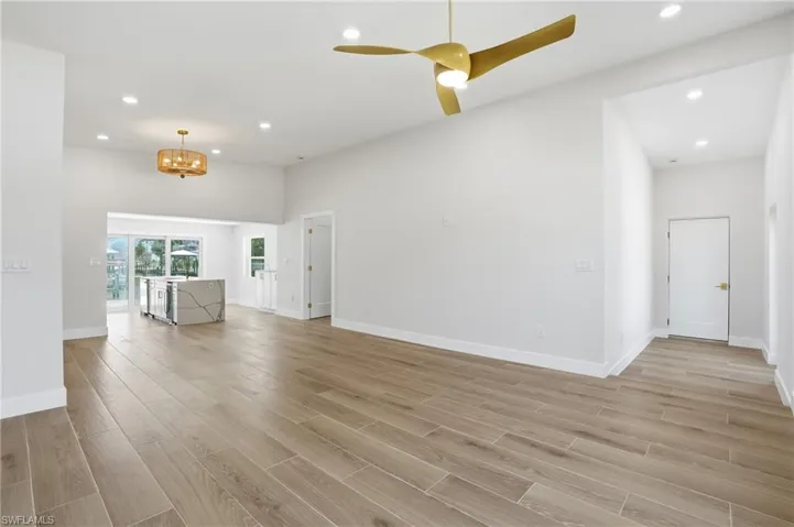 Spacious living area featuring light wood-look flooring, recessed lighting, and a modern ceiling fan - Virtually Edited Image